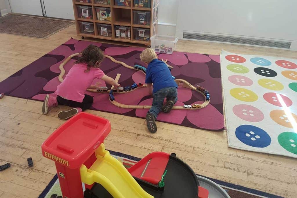 Children playing with train set on colorful carpet at Whitley Community Preschool.